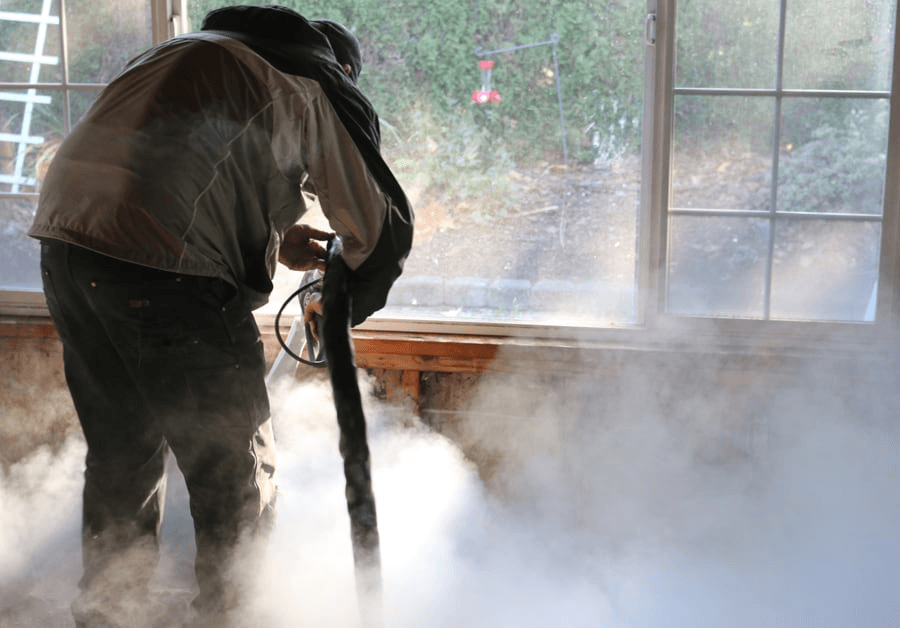 Technician lifting soot and char from wood beams with a dry-ice blaster inside containment